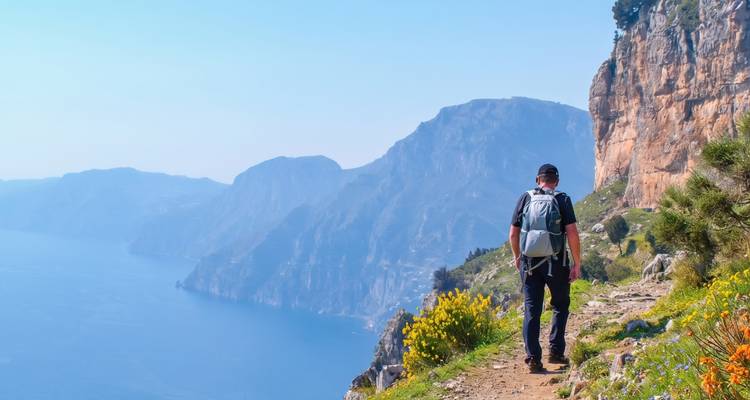 Voyageur à dos léger sur un sentier pittoresque en corniche dominant un littoral azuré et des fleurs sauvages