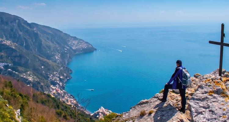 Le trekker se tient près d'une croix dominant une vue panoramique de la côte amalfitaine en contrebas.