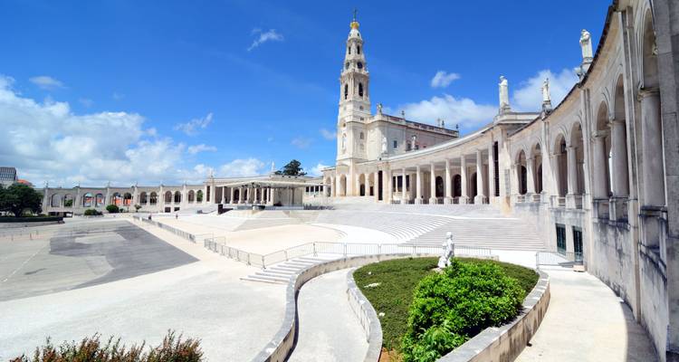 Vista amplia de la gran basílica blanca y las majestuosas columnatas del Santuario de Fátima bajo un cielo azul brillante.
