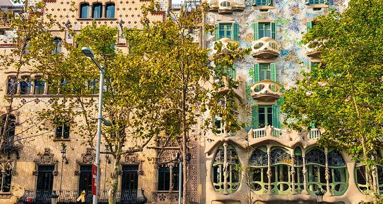 Vue de rue de deux bâtiments modernistes ornés sur le Passeig de Gràcia de Barcelone encadrés par des arbres feuillu