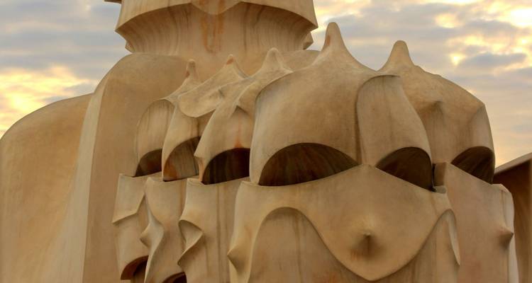 Gros plan sur les cheminées en grès sculptées ressemblant à des guerriers masqués au sommet de la Casa Milà de Gaudí sur un ciel doux.