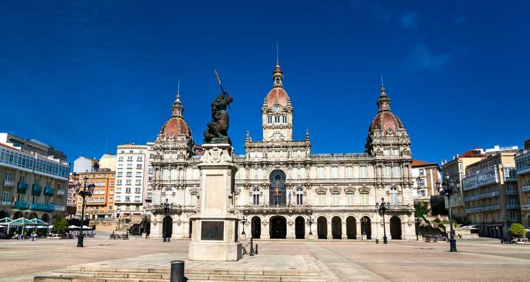 Das imposante Rathaus mit drei Kuppeltürmen dominiert einen offenen Platz mit einer zentralen Statue unter tiefblauem Himmel.