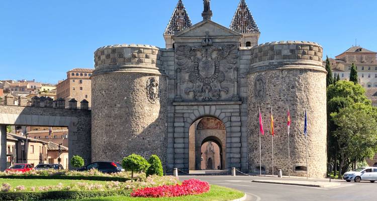 Puerta de entrada de piedra Puerta de Bisagra en Toledo con escudos de armas, torreones y visitantes cerca.