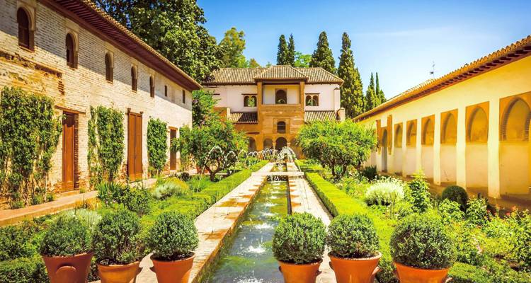 Weelderige Generalife-tuinen met symmetrische hagen en fonteinen in het Alhambra-complex.