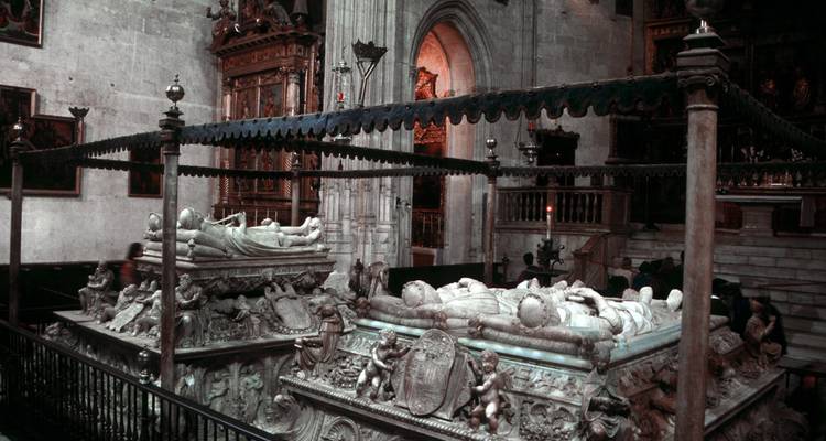 Tumbas reales con poca luz adoradas con efigies esculpidas y tallas ornamentadas dentro de una capilla gótica.