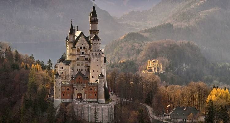 El icónico Castillo de Neuschwanstein encaramado en una colina boscosa con montañas de fondo bajo la suave luz de la tarde