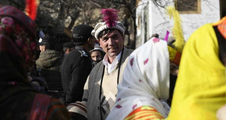 Mann in traditioneller Chitrali-Mütze mit Feder, der unter Festivalteilnehmern in Winterkleidung lächelt.