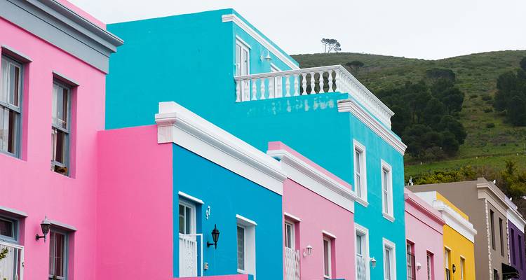 Fila de casas pintadas de colores brillantes en el histórico barrio Bo-Kaap de Ciudad del Cabo contra una ladera verde.