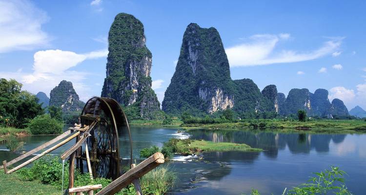 Dramatische Karstgipfel, die sich neben einem ruhigen Fluss mit einem alten hölzernen Wasserrad in Yangshuo erheben.