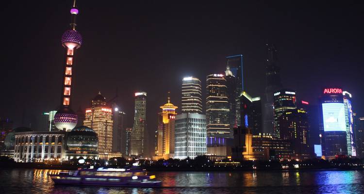 El horizonte nocturno de Pudong en Shanghái con la Torre de la Perla Oriental iluminada y rascacielos coloridos reflejándose en el río Huangpu.