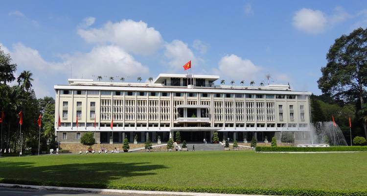 Voorkant van het Reunificatiepaleis in Ho Chi Minhstad met de Vietnamese vlag wapperend boven verzorgde grasvelden.