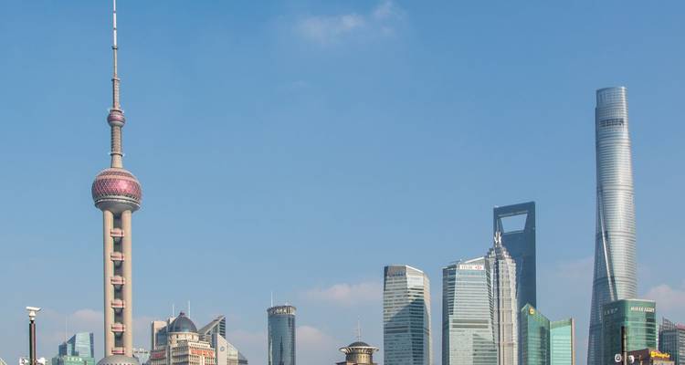 Moderne skyline van Shanghai met de Oriental Pearl Tower en omringende wolkenkrabbers tegen een heldere blauwe lucht.