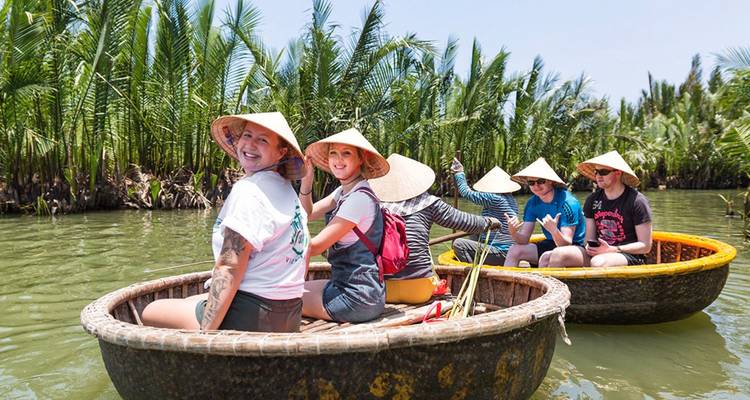 Des voyageurs souriants naviguant en barques rondes traditionnelles dans un canal bordé de palmiers