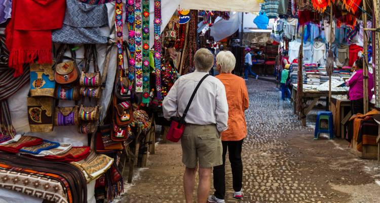 Älteres Ehepaar schlendert durch einen farbenfrohen Textil- und Handwerkssuk auf einer Kopfsteinpflasterstraße.