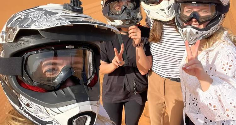 Gruppen-Selfie mit Motocross-Helmen auf Wüstensand mit Friedenszeichen.