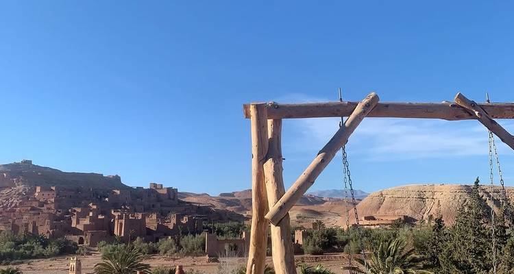 Houten schommelframe met uitzicht op het aarden dorp Ait Benhaddou tegen een strakblauwe hemel.