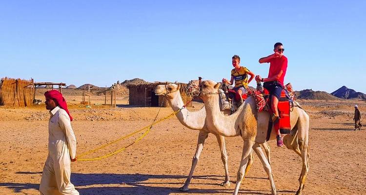 El guía lleva a dos niños montando camellos a través del desierto arenoso con colinas rocosas