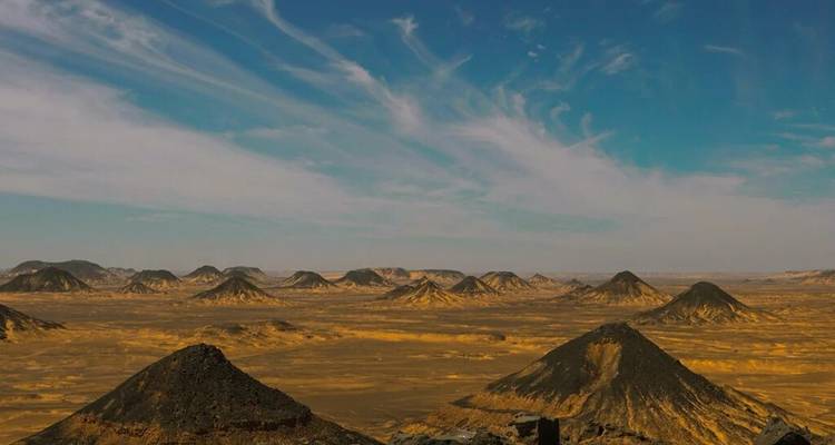 Serie de conos volcánicos negros elevándose desde el desierto dorado bajo un cielo rayado