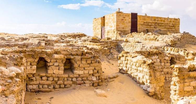 Ruinas antiguas de ladrillos de barro parcialmente enterradas en arenas del desierto bajo un cielo azul