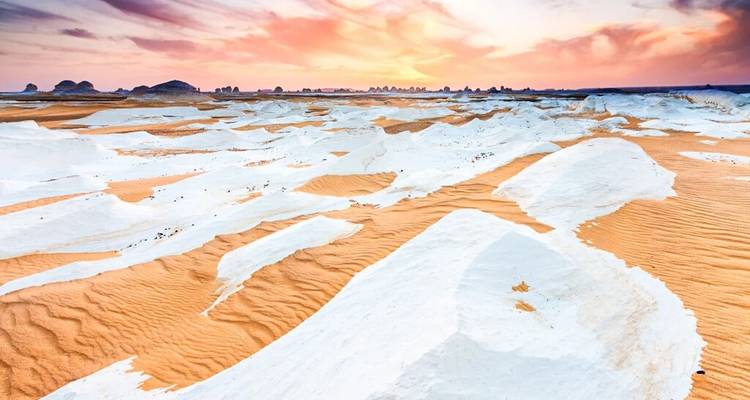 Formaciones de tiza blanca contrastando con arena naranja bajo un cielo de atardecer vibrante