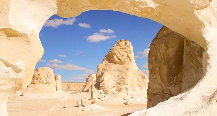 Arco de roca natural enmarcando formaciones de piedra caliza beige contra un cielo azul
