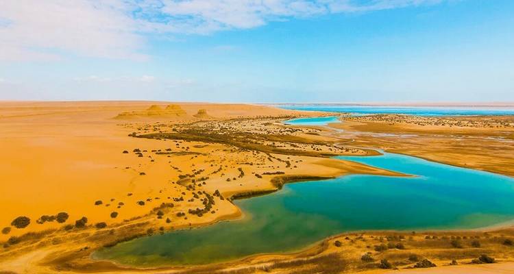 Luchtfoto van een turquoise rivier die zich door een uitgestrekte gouden woestijn slingert