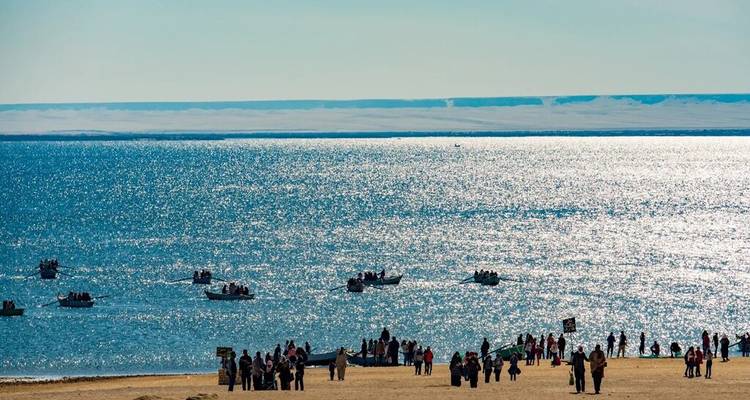 Glitterend meer met kleine roeibootjes en groepen mensen op het zandige strand