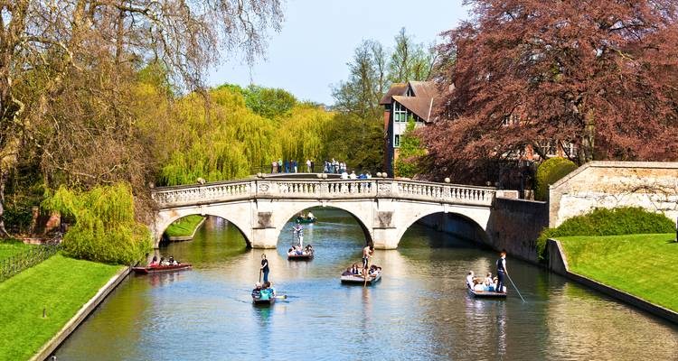 Les touristes naviguent en barque le long de la rivière Cam sous un élégant pont de pierre entouré de feuillage printanier à Cambridge.