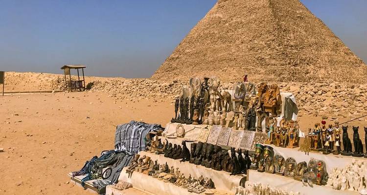 Des étals de souvenirs présentant des figurines et des objets artisanaux devant une pyramide.