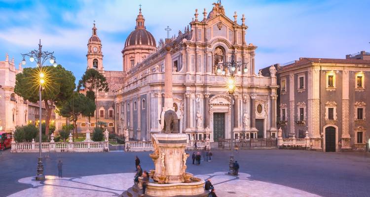 Abendliche Ansicht des Doms von Catania und des Elefantenbrunnen, die in sanftem Licht erstrahlen, mit einigen Einheimischen auf dem Platz.