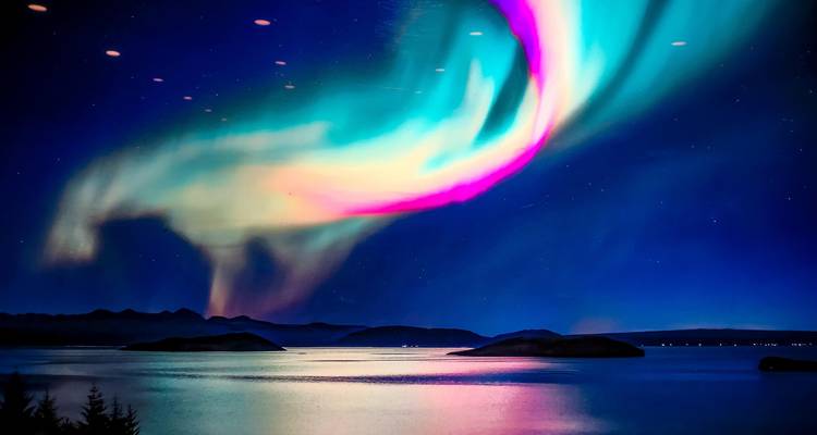 Des arcs spectaculaires d'aurores boréales aux couleurs néon s'étendent sur des eaux calmes et des îles lointaines la nuit.