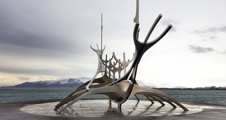 La sculpture moderne Sun Voyager se dresse au bord de la mer avec des montagnes enneigées sous des ciels gris.