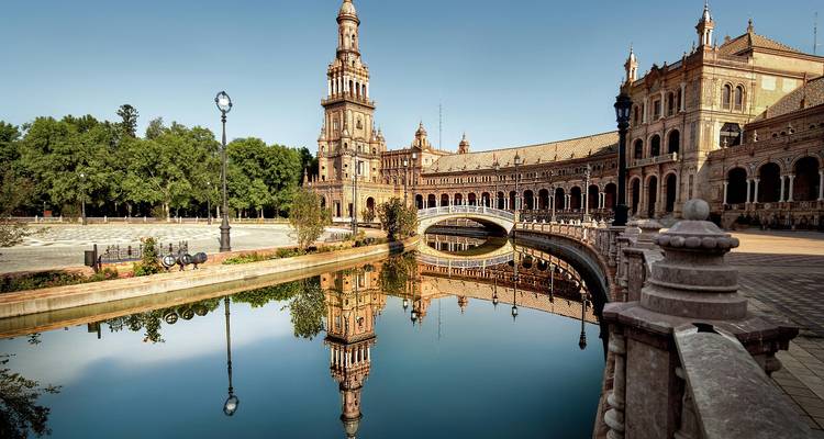 Elegante Plaza de España con puentes arqueados reflejados en un canal tranquilo bajo un cielo azul despejado