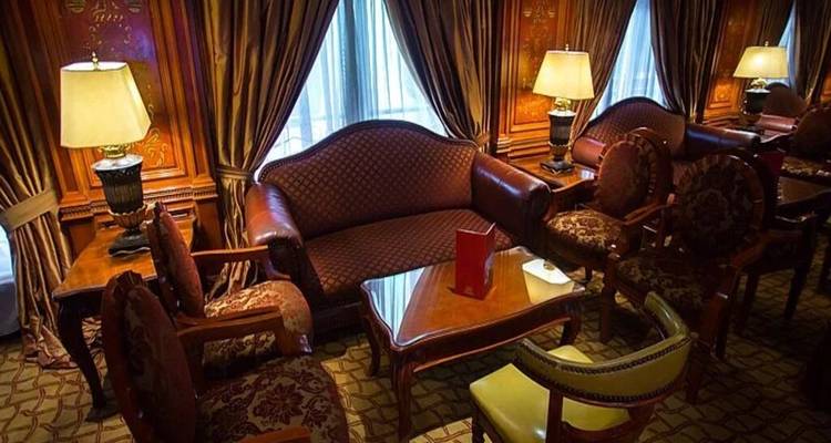 Elegante salón con paneles de madera, sofás de cuero, cortinas ornamentales y lámparas de mesa.