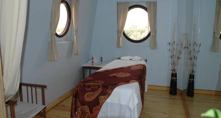 Eenvoudige massagekamer aan boord met een behandelbed naast twee ronde patrijspoorten
