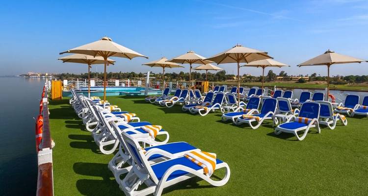 Ruim groen grasveld zonneterras met blauwe ligbedden en parasols met uitzicht op een brede rivier