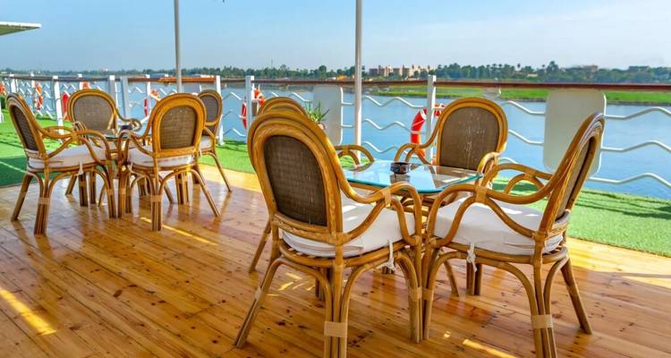 Houten terras met rieten eetkamerset met uitzicht op een rustige rivier en palmbomen aan de oever