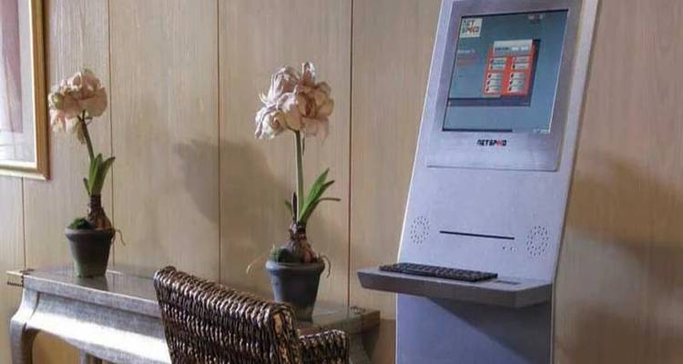 Kleine hoekje in de lobby met twee orchideeën in potten en een zelfbedienings-computerkiosk