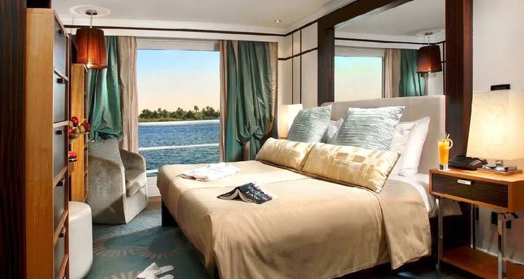 Cabine de croisière avec lit double et fenêtre panoramique sur la rivière, jus de fruit et livre sur le lit