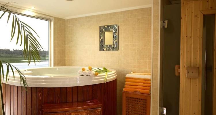 Privéspakamer met een rond jacuzzibad, saunacabine en opgerolde handdoeken.