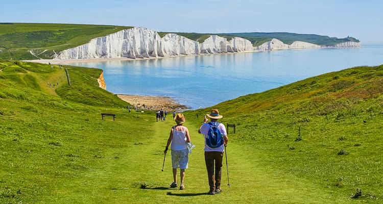 Zwei Wanderer mit Stöcken geniessen den grünen Wanderweg auf der Klippe mit Blick auf die weissen Seven Sisters