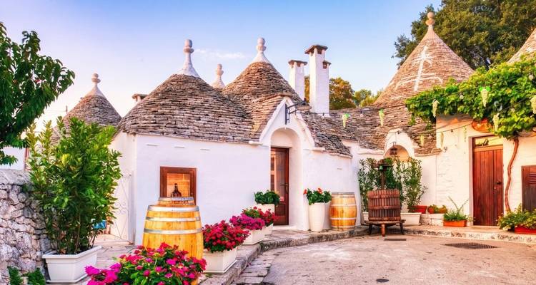 Jolie cour avec des maisons trulli bien conservées, des tonneaux en bois et des jardinières sous une douce lumière du soir.