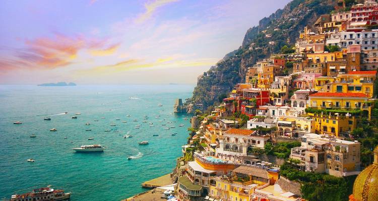 Das lebendige Dorf Positano an der Steilküste mit pastellfarbenen Häusern, die zum türkisfarbenen Tyrrhenischen Meer hinabfallen, das bei Sonnenuntergang mit Booten gefüllt ist.