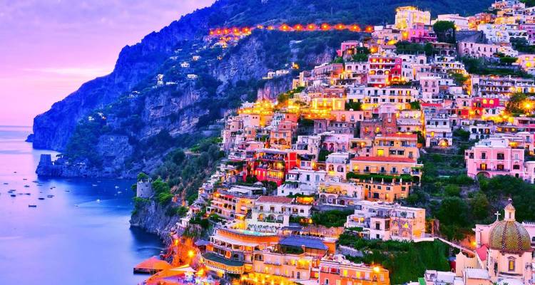 Les lumières du soir illuminent les maisons empilées de Positano qui dégringolent vers une mer calme sous un ciel crépusculaire pourpre.