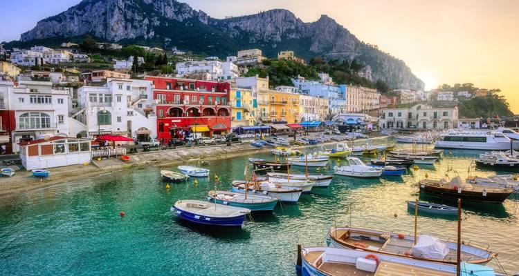 Escena colorida del puerto de Capri al atardecer con botes en agua cristalina y edificios en la ladera.