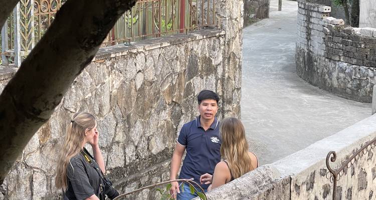 Guía hablando con dos viajeros en un callejón estrecho de piedra rodeado de muros altos.
