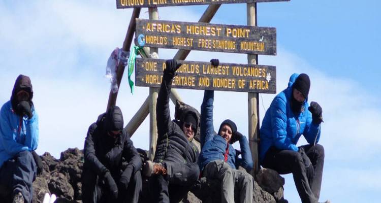 Des alpinistes en tenue d'hiver célébrant au panneau du sommet Uhuru sur le Mont Kilimandjaro.