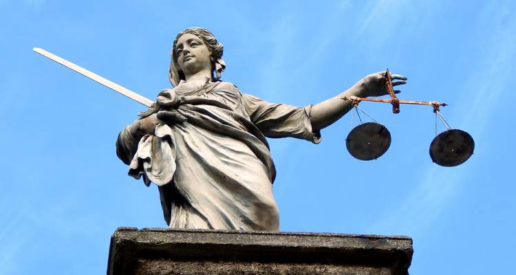 Statue de pierre de la Dame de la Justice tenant une épée et des balances équilibrées sur un ciel bleu dégagé