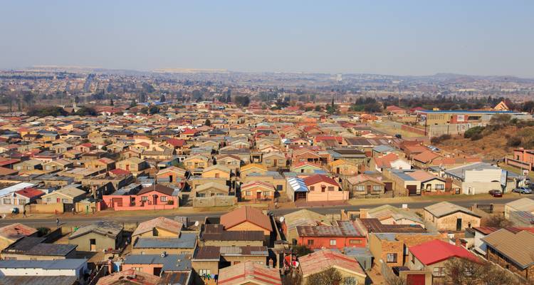 Vue panoramique de logements bas densité dense à travers le township de Soweto sous un ciel brumeux.