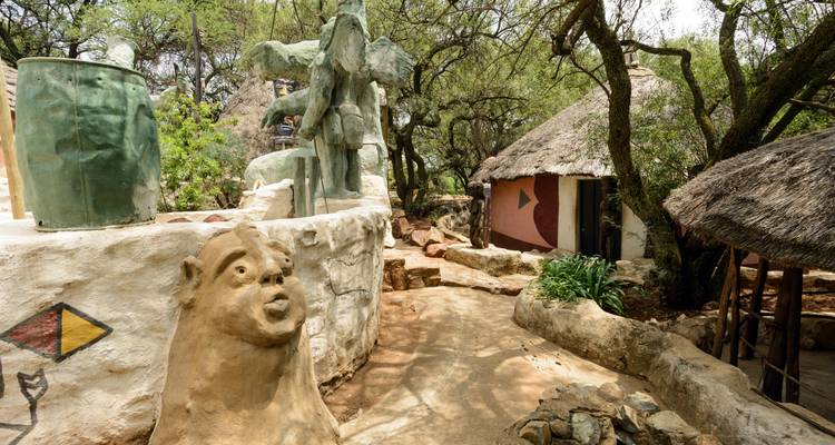 Village culturel artistique avec des sculptures en argile, des huttes au toit de chaume et des arbres ombragés.
